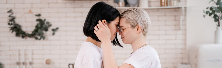 side view of young lesbian couple hugging in kitchen, banner