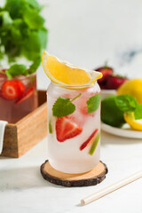 A refreshing summer drink with strawberries, lemon and mint in a glass on a light background. Strawberry lemonade