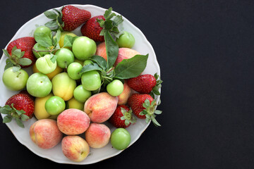 Top view of Fresh summer fruits, plum, peach, apricot, strawberry in plate on black background, copy space, food concept.