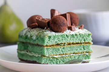 Delicious rectangular green cake on a white plate decorated with pieces of chocolate and brown candies.