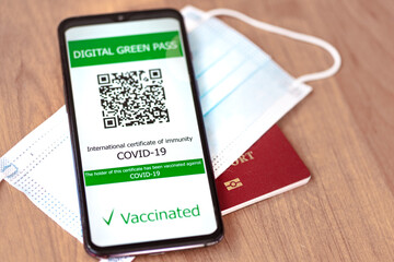 Digital Green Pass concept: Smartphone over a passport and a surgical mask on a table