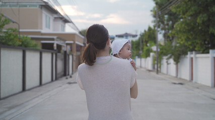 young happy asian woman mother walking outdoor holding baby infant around neighbor. woman in medical face mask walk village street in evening during covid 19. natural authentic.