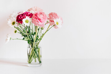 A bouquet of fresh spring flowers in a glass vase on a white table.