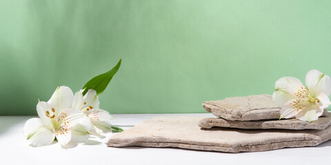Background for cosmetic products of natural green color. Stone podium with white flowers. Front...