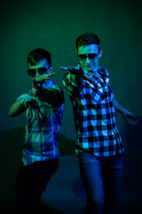 Fototapeta na wymiar Two young men in plaid shirts dance in the studio with multicolored light