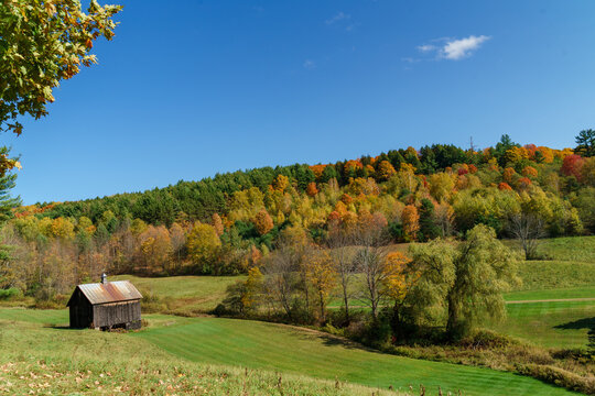 A solitary old barn sitting before a hill of vibrant foliage as Autumn falls. Vermont, United States