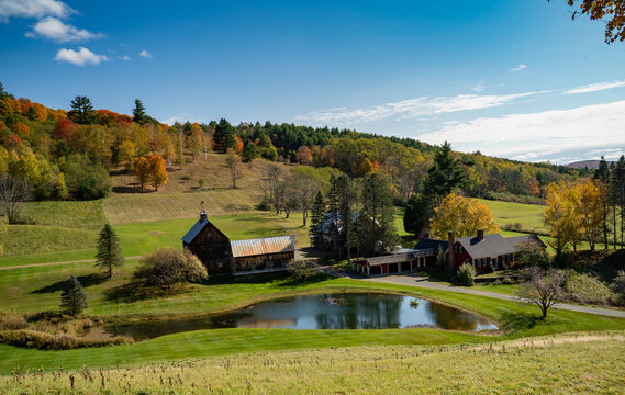 A farm house built beside the quiet pond as the beautiful foliage turn the hill into a colorful backdrop in Autumn. Vermont, United States