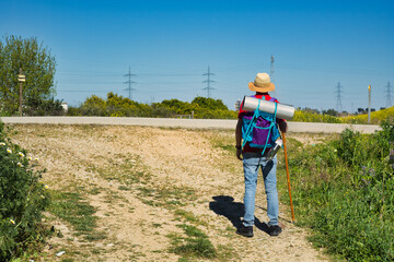 Pilgrim walking the road to Santiago with backpack, walking stick and hat.