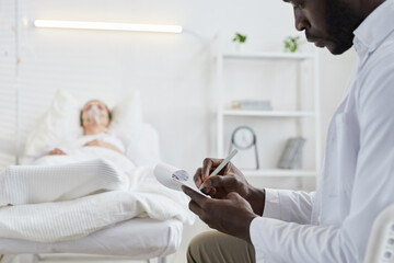 Obraz premium Close-up of African doctor writing prescription in medical card for patient who lying on hospital bed