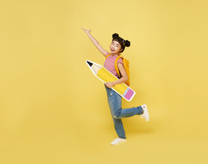 Back to school. Happy cute asian child with big backpack holding pencil on yellow background....