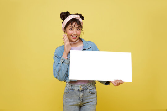 Excited Asian Teen Girl Holding Blank Speech Bubbles On Yellow Background.