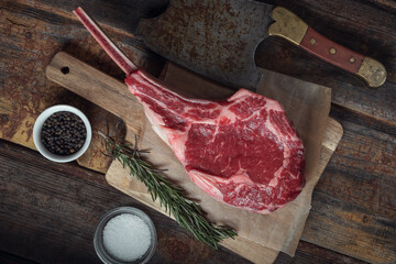 Tomahawk steak, rosamarine, spices and an old meat cleaver on a wooden table. Top view.