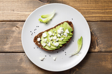 Whole grain rye bread toast with goat cheese and avocado on wooden table background. Healthy avocado open sandwich for breakfast or lunch. Flat lay, top view, copy space