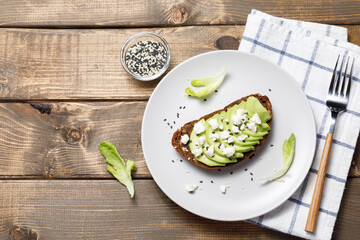 Whole grain rye bread toast with goat cheese and avocado on wooden table background. Healthy avocado open sandwich for breakfast or lunch. Flat lay, top view, copy space
