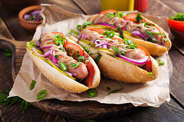 Hot dog with  pickles, tomato and lettuce on wooden background. Hotdog, american cuisine.