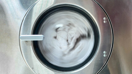 Towels are spinning inside the front door of stainless steel industrial washing machine. Shot taken in the factory.