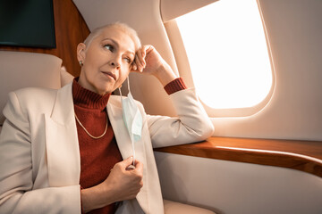 Mature businesswoman taking off medical mask in private jet
