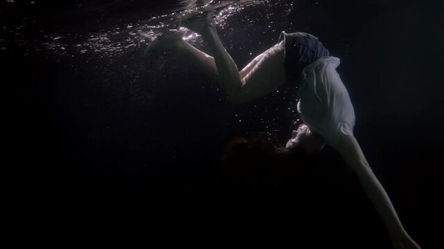 adult woman in clothes under the water in the pool spinning in slow motion