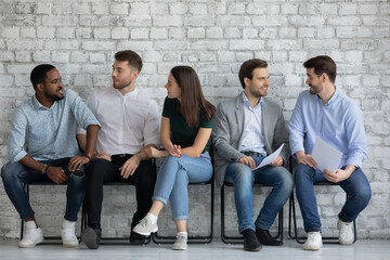 Vacancy applicants talking, discussing employment and hiring, waiting appointment with employer in corridor. Queue of candidates expecting job interview, holding resume, sitting on chairs, chatting