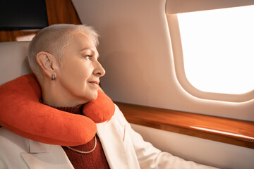 Mature businesswoman in neck pillow looking at plane window