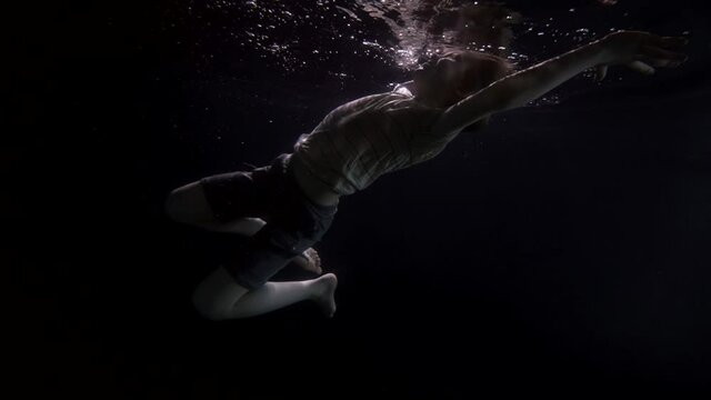 slow motion boy child underwater in shorts and tank top floating in the water like in a dream