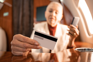Credit card in hand of businesswoman with smartphone on blurred background in airplane