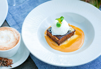 Chocolate cake with a ball of white ice cream decorated with mint leaf and caramel syrup is served on a large white plate in the restaurant. Restaurant menu.
