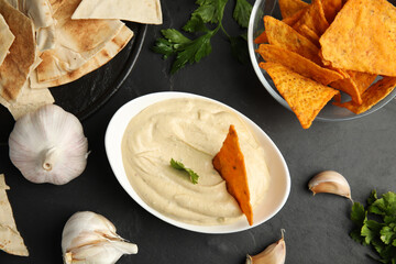 Delicious hummus with nachos and parsley on black table, flat lay