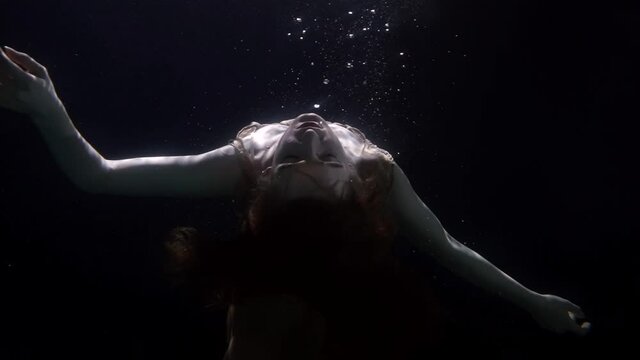 slowed down underwater portrait of woman facing the light floats up unconscious