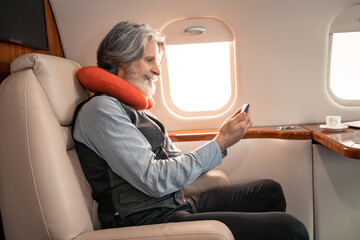 Side view of businessman in neck pillow using smartphone near coffee in private jet