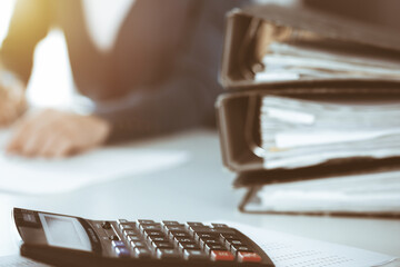 Calculator and binders with papers are waiting to be processed by business woman or bookkeeper working at the desk in office back in blur. Internal Audit and tax concept