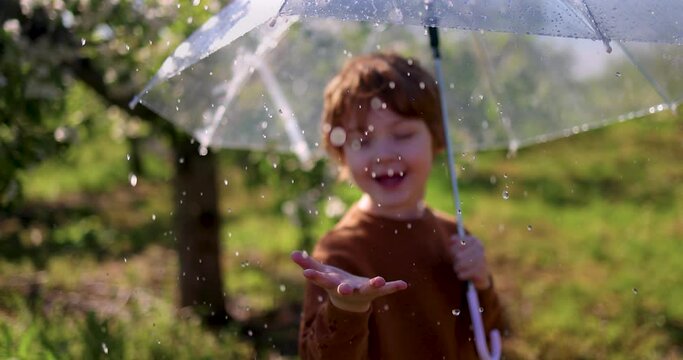 hand of cheerful baby boy catching the rain drops, that are falling from umbrella in spring garden at sunny summer day