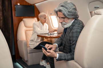 Obraz premium Businessman using smartphone near blurred businesswoman in plane