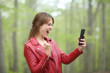 Amazed woman celebrating success checking phone in a park
