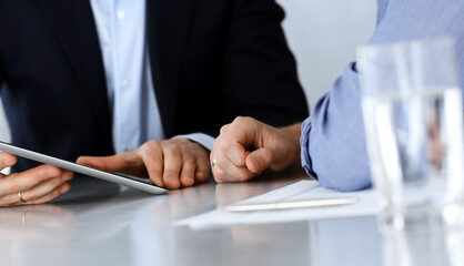 Business people using tablet computer while working together at the desk in modern office. Unknown businessman or male entrepreneur with colleague at workplace. Teamwork and partnership concept