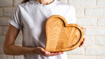 Fototapeta na wymiar Wooden plate in shape of heart, Heart shaped wooden plate in female hands, close up.