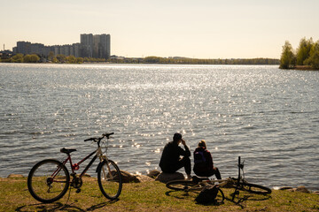 Obraz premium Couple of cyclists sit on the shore of the lake in spring in the park