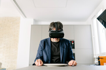 Stylish adult male pretending to eat in a modern kitchen experiencing virtual reality on the empty...