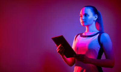 Innovative technology. Neon banner. Crypto business. AI software. Cyborg woman with tablet in bright pink blue fluorescent light isolated on purple empty space background.
