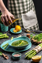 Spring detox Asparagus green cream soup in bowls. Cook hand sprinkling olive oil. Clean eating, dieting, vegan, vegetarian, healthy food concept
