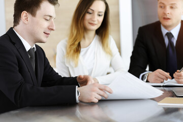 Fototapeta premium Business people or lawyers discussing questions at meeting in sunny office. Unknown businessman and woman with colleague sitting and working at the glass desk
