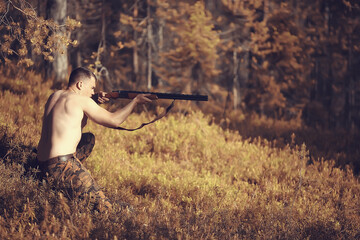 hunting man / hunter with a gun hunting in the autumn forest, yellow trees landscape in the taiga