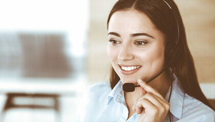 Brunette female customer service representative in a headset is consulting clients online. Call center and business people concept