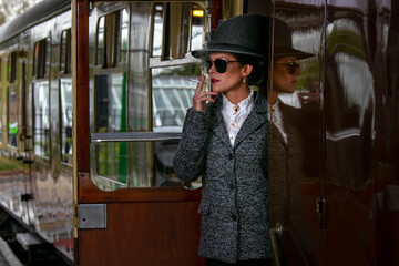 Beautiful female in vintage 1920s costume smoking cigarette while leaving train at train station
