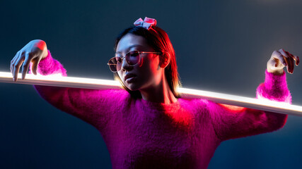 Cyberpunk fashion. Neon light people. Futuristic portrait. Glamour Asian girl in pink in sunglasses in red color glow with illuminated white LED lamp stick isolated on dark night blue.