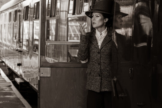 Beautiful female in vintage 1920s costume smoking cigarette while leaving train at train station