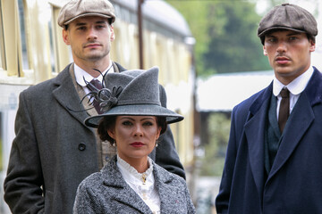 Gangster family of 1920s standing on railway station platform with train in the background