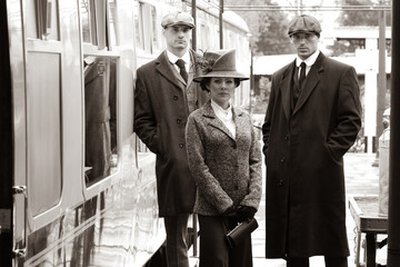 Gangster family of 1920s standing on railway station platform with train in the background - obrazy, fototapety, plakaty