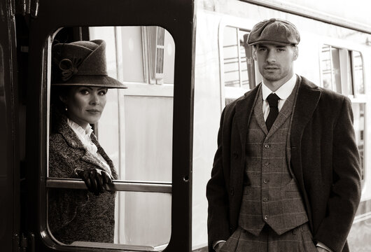 Beautiful woman dressed in vintage 1920s costume arriving by train and greeted by her bodyguard