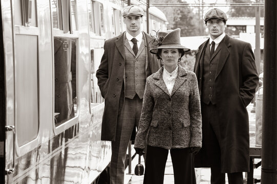Gangster family of 1920s standing on railway station platform with train in the background